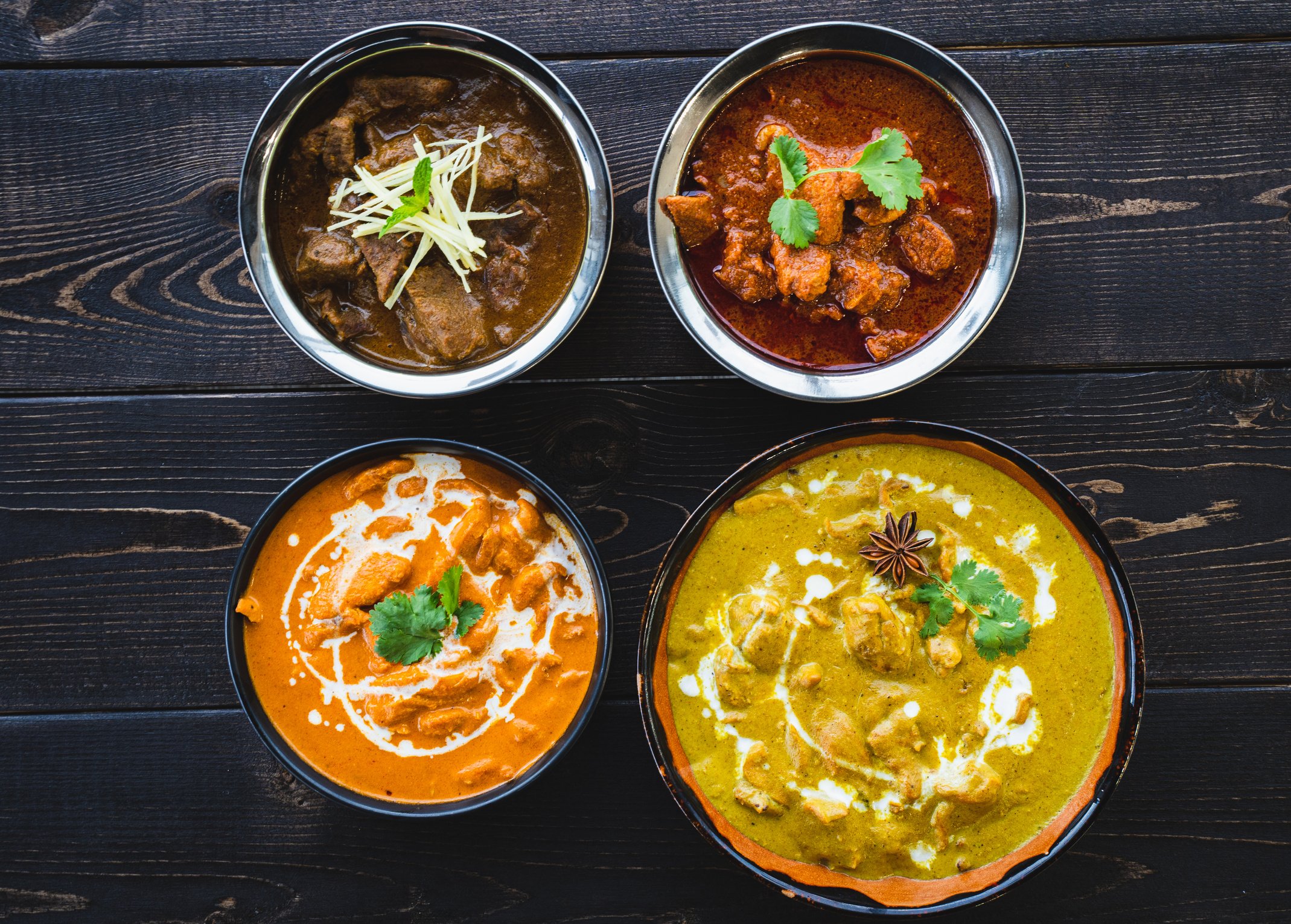 Various types of Hotel Daawat Indian curries decoratively arranged in bowls on a wooden table